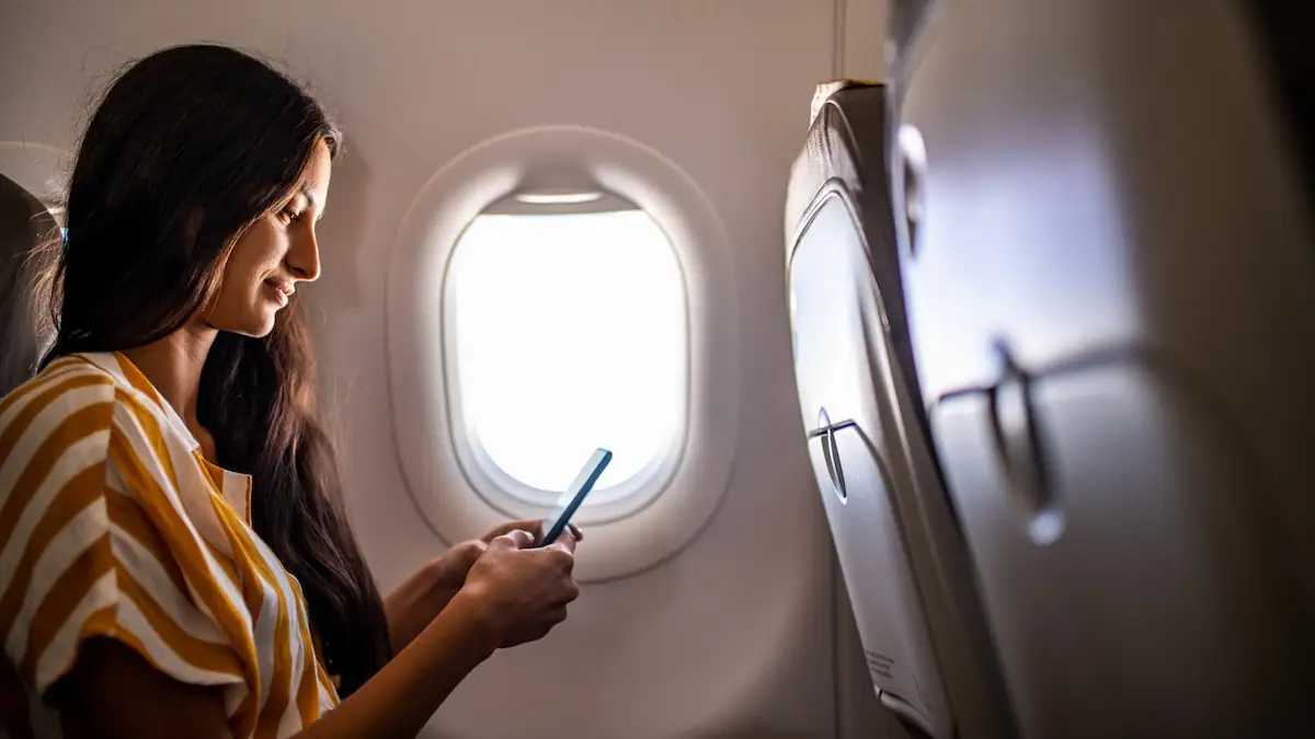 Powerbank im Flugzeug: Frau sitzt mit Handy an Bord eines Flugzeugs