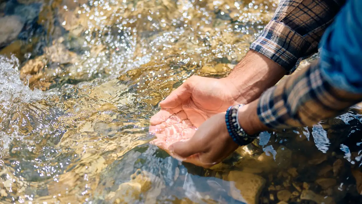Mann schöpft mit den Händen Wasser aus einem Bach