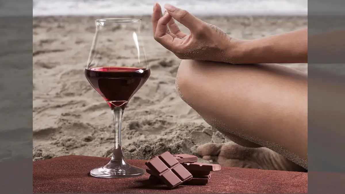 Sirt Diät: Frau macht Yoga am Strand neben einem Glas Rotwein und einer Tafel Schokolade