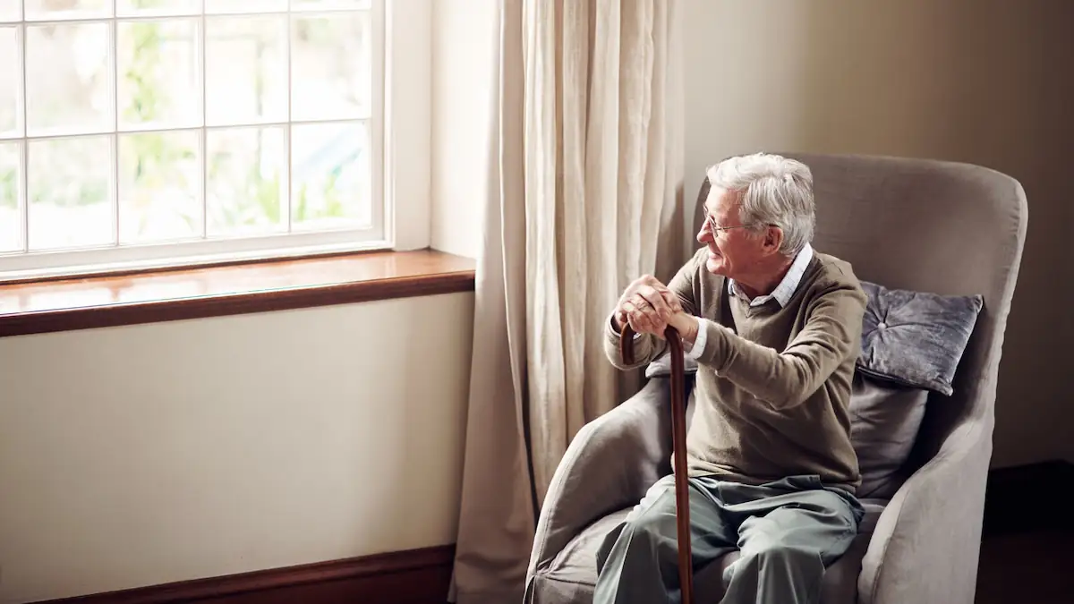 Alzheimer Symbolbild: Alter Mann sitzt mit Gehstock am Fenster