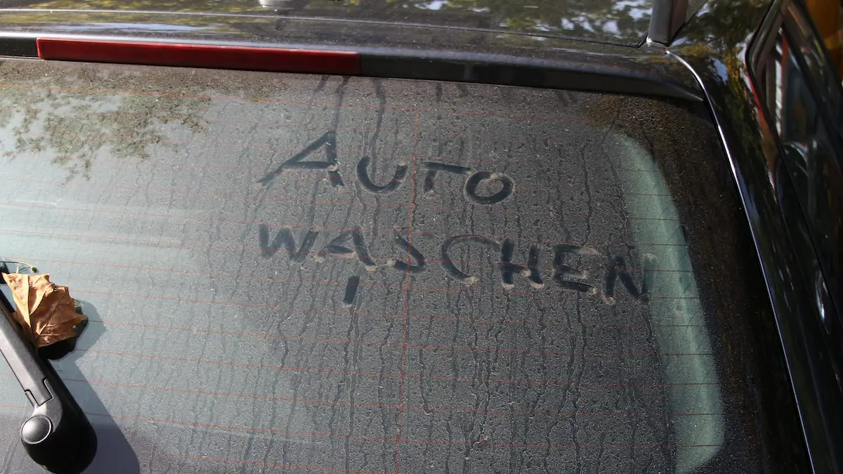 „Auto waschen“-Schriftzug auf einer dreckigen Frontscheibe