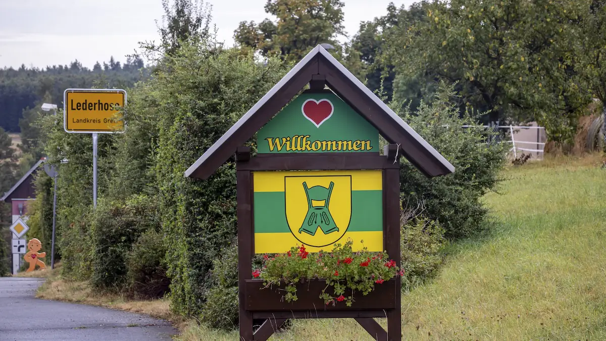 Lustige Ortsnamen: Ortsschild der Gemeinde Lederhose im Landkreis Greiz, Wappen der Gemeinde. Witziger Ortsname von Lederhose, Thüringen, Deutschland, 