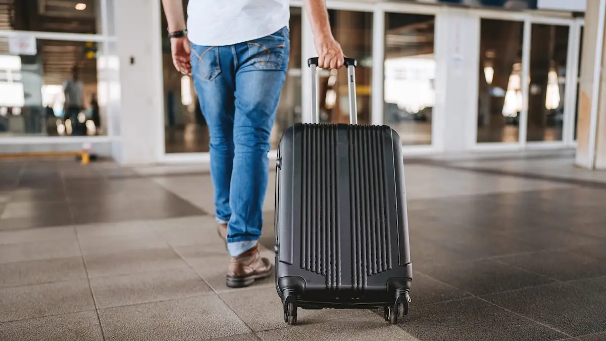 Mann rollt einen schwarzen Koffer hinter sich her