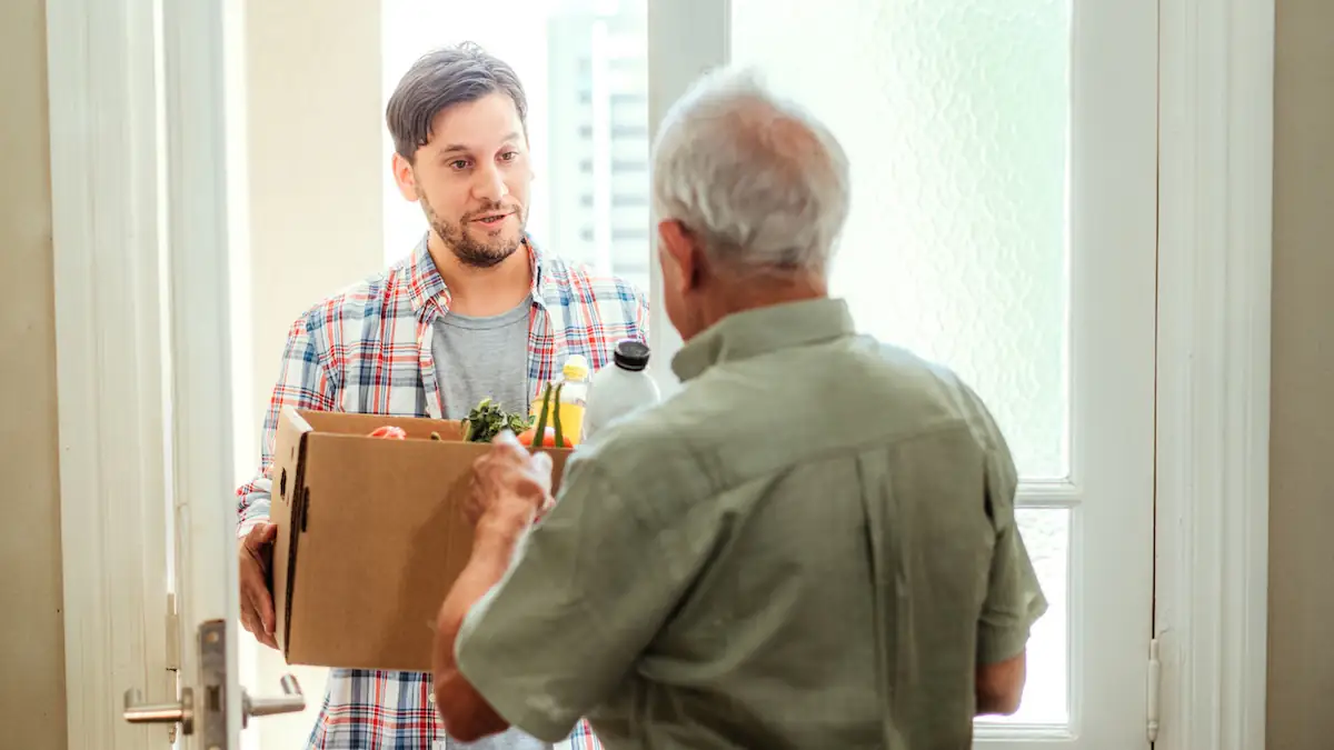 Discounter Penny stellt Lieferdienst ein (Symbolbild): Junger Mann liefert Kiste mit Lebensmitteln an einen Senioren