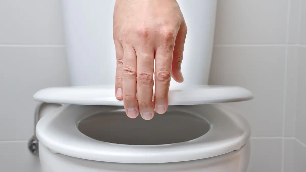 Hand eines Mannes, der den Deckel einer Toilette im Badezimmer schließt