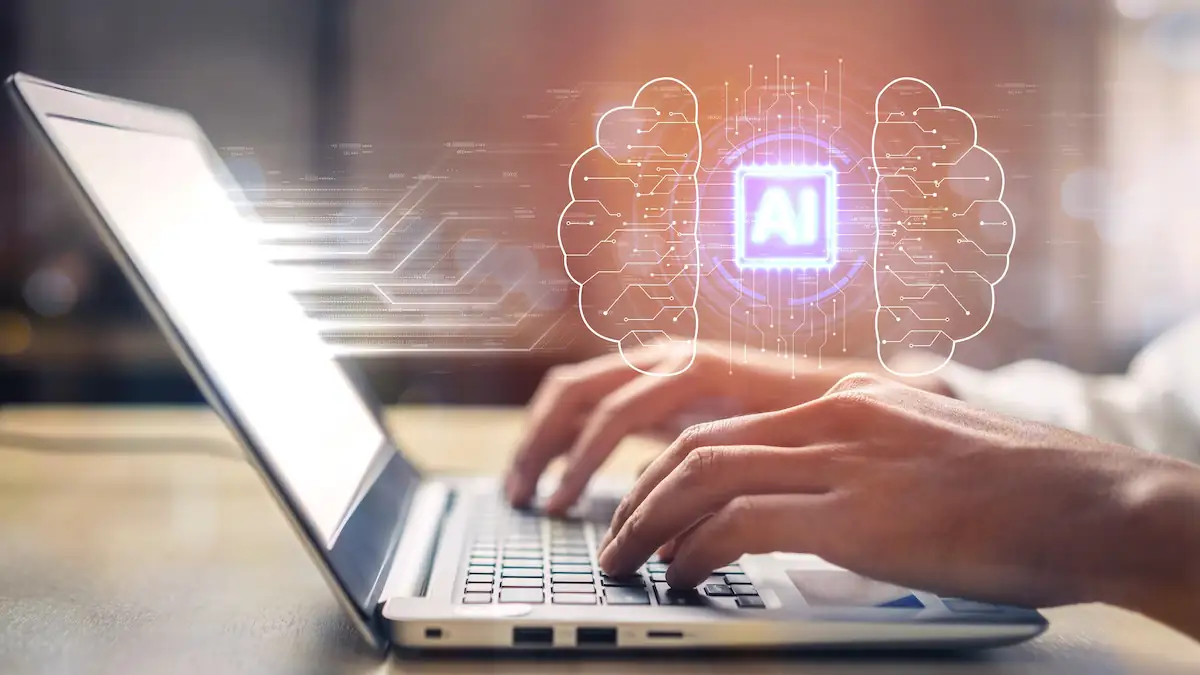 KI-Chatbot Symbolbild: Jemand tippt an einem Laptop, über dem ein Gehirn mit den Buchstaben „AI“ für „Artificial Intelligence“ stehen