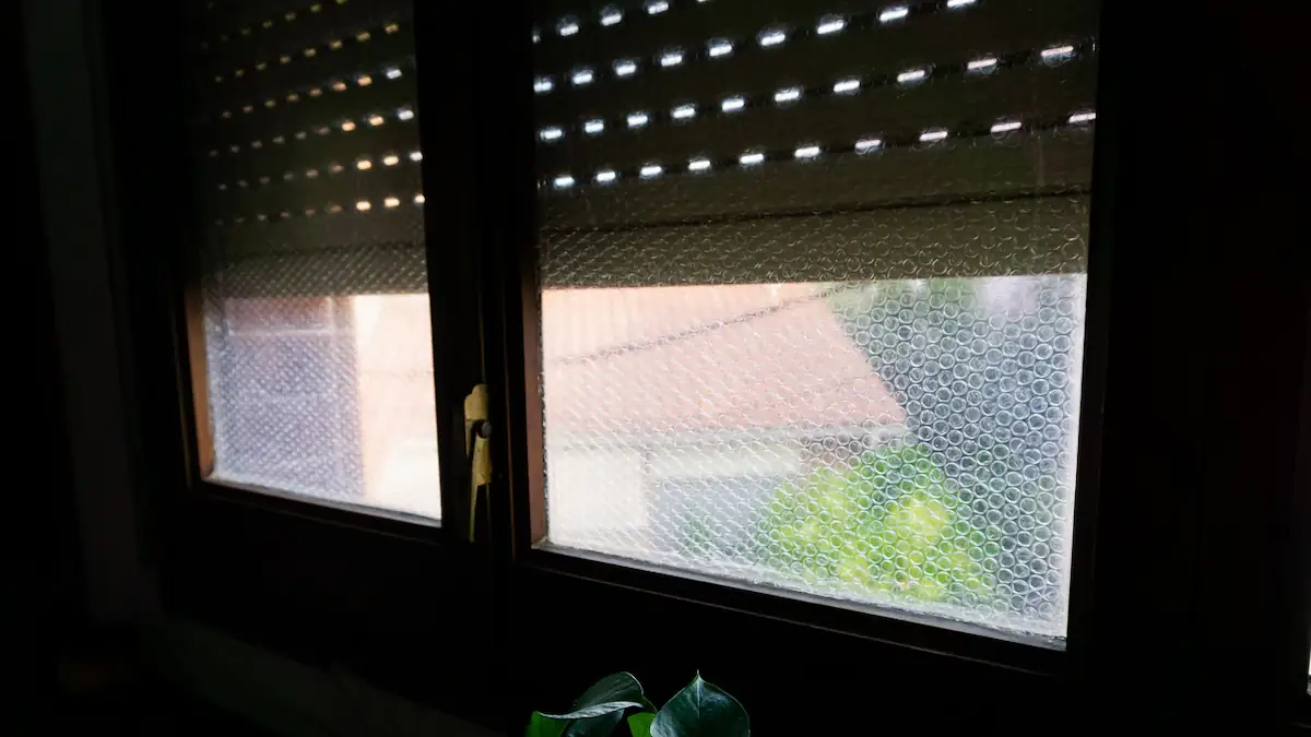 Fenster mit halb geschlossenen Rollläden, das mit Luftpolsterfolie verklebt ist