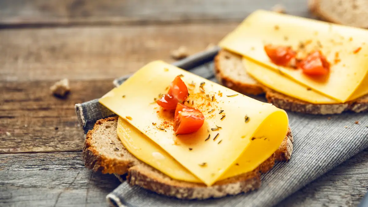 Käse soll laut Studie Demenzrisiko reduzieren: Zwei SCheiben Brot nebeneinander, darauf jeweils eine Scheibe Käse und klein geschnittene Tomaten