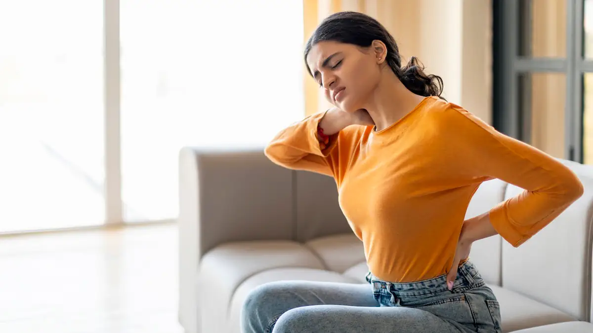 Junge Frau mit Rückenschmerzen hält sich Nacken und Kreuz