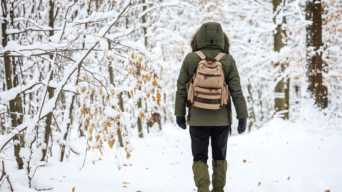 Eine Person mit grüner Winterjacke und Kapuze läuft in Schneelandschaft