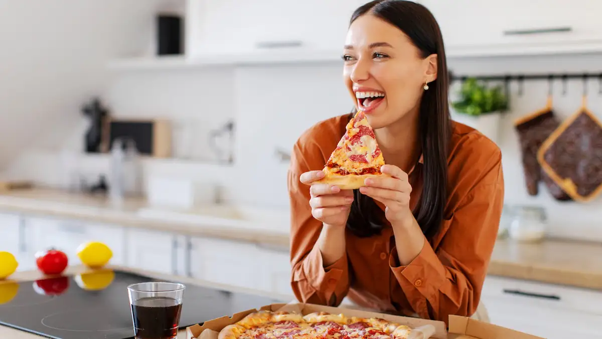 Frau isst glücklich lachend ein Stück Pizza