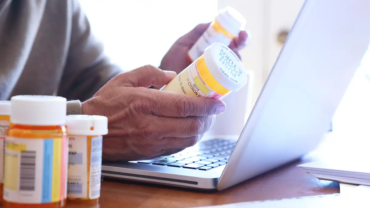 Arzneimittel bei Amazon bestellen: Person sitzt mit Medikamentenschachteln vor einem Laptop