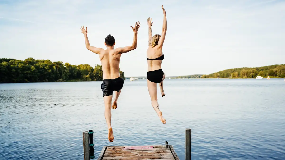 Symbolbild Badeverbot: Ein Mann und eine Frau springen in Badekleidung von einem Steg ins Wasser