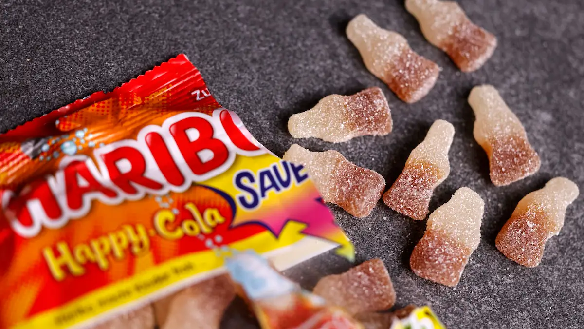 Haribo Tüte Happy Cola sauer mit einigen ausgepackten Gummibärchen in Colaflaschen-Form