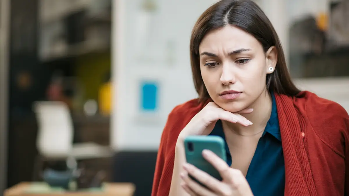 Symbolbild Tinder Filter für Körpergröße: Frau schaut skeptisch auf ihr Smartphone