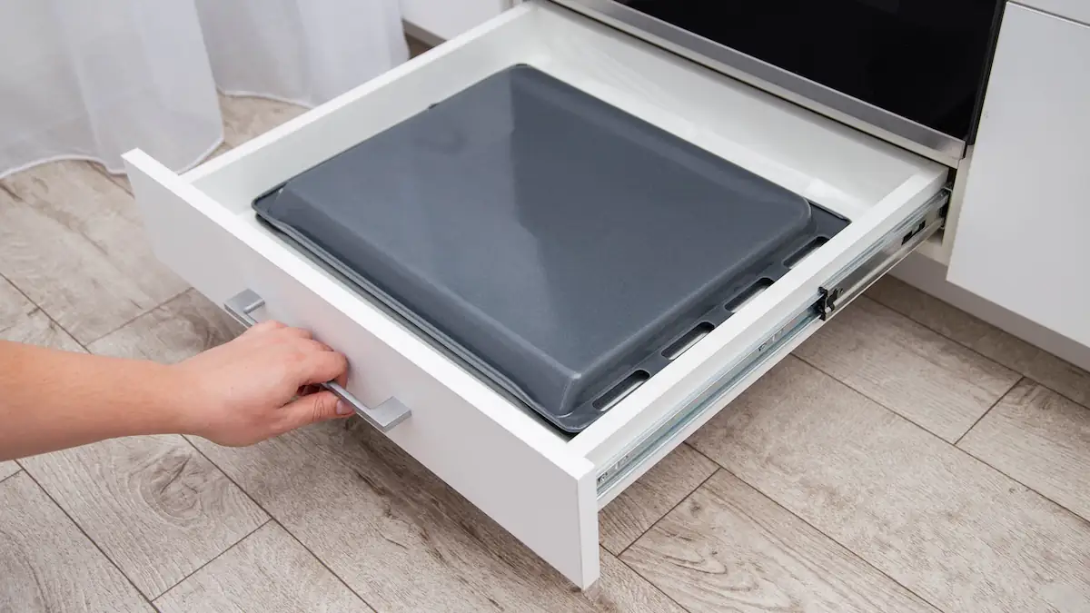 Mann ziht die Schublade unter einem Backofen heraus, in der sich in ein Backblech befindet