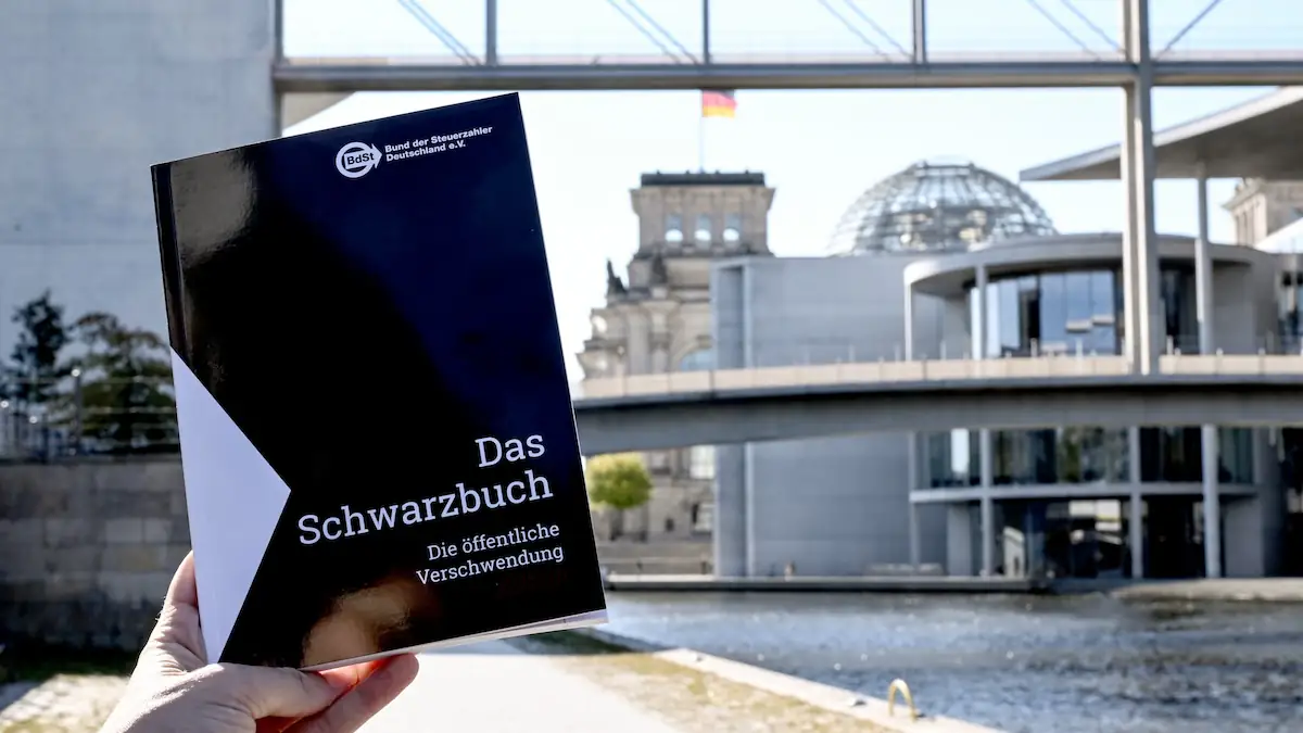 Das Schwarzbuch 2025/26 vom Bund der Steuerzahler in wird vor das Reichstagsgebäude gehalten. Das Schwarzbuch listet Beispiele auf, wo aus Sicht des Steuerzahlerbunds Steuergelder verschwendet wurden.