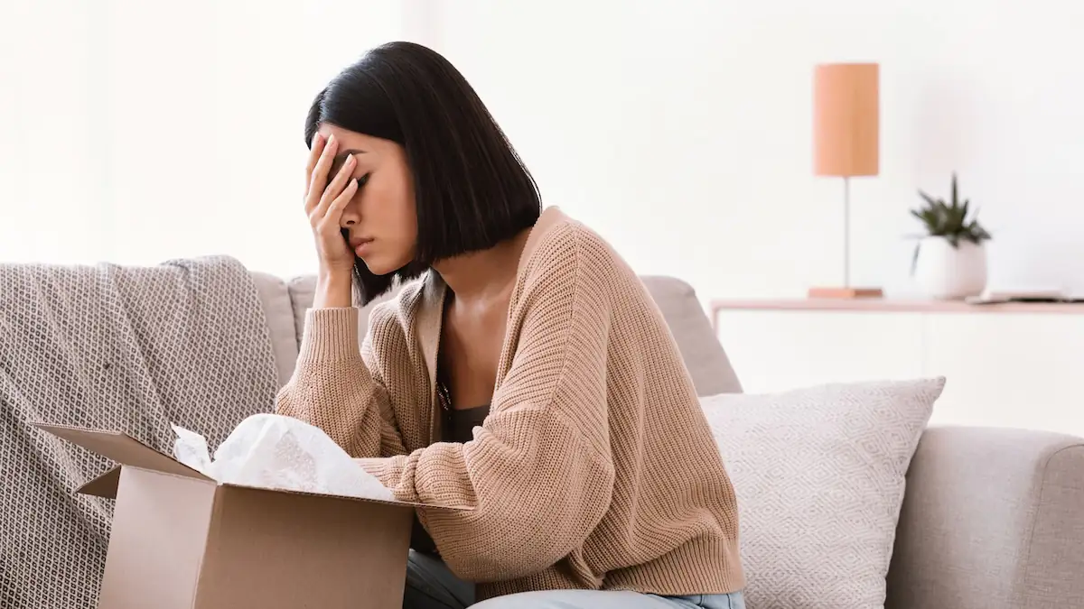 Pakete für Nachbarn annehmen: Frau stützt schockiert das Gesicht in die Hand, nachdem sie ein Paket geöffnet hat