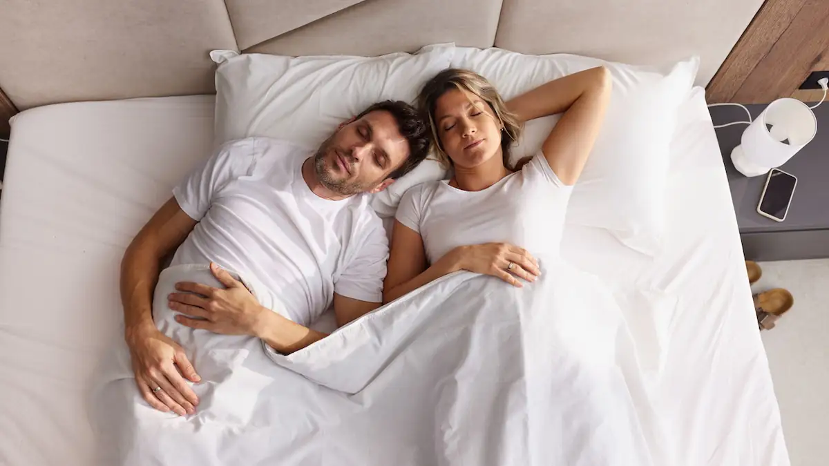 Schlafposition: Junges Paar liegt zusammen auf dem Rücken im Bett und schläft