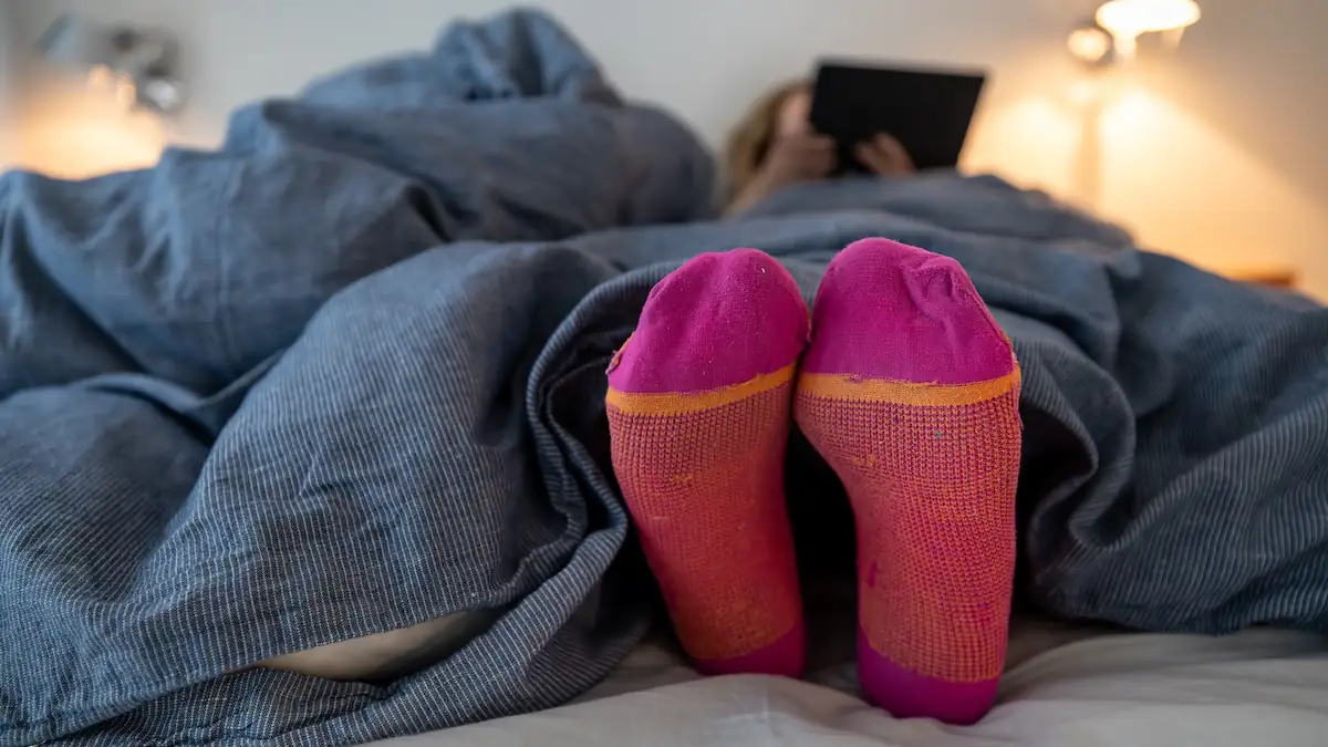 Frau trägt beim Lesen im Bett bunte Wollsocken