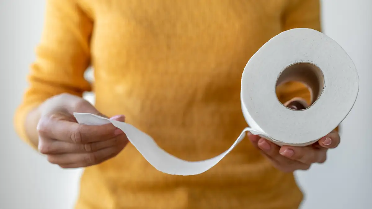 Eine Frau in einem gelben Pullover hält eine Rolle Toilettenpapier in der Hand