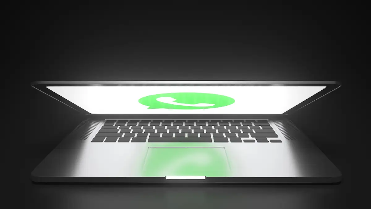 WhatsApp-Logo auf einem halb geschlossenen, hellleuchtenden Laptop in dunkler Umgebung